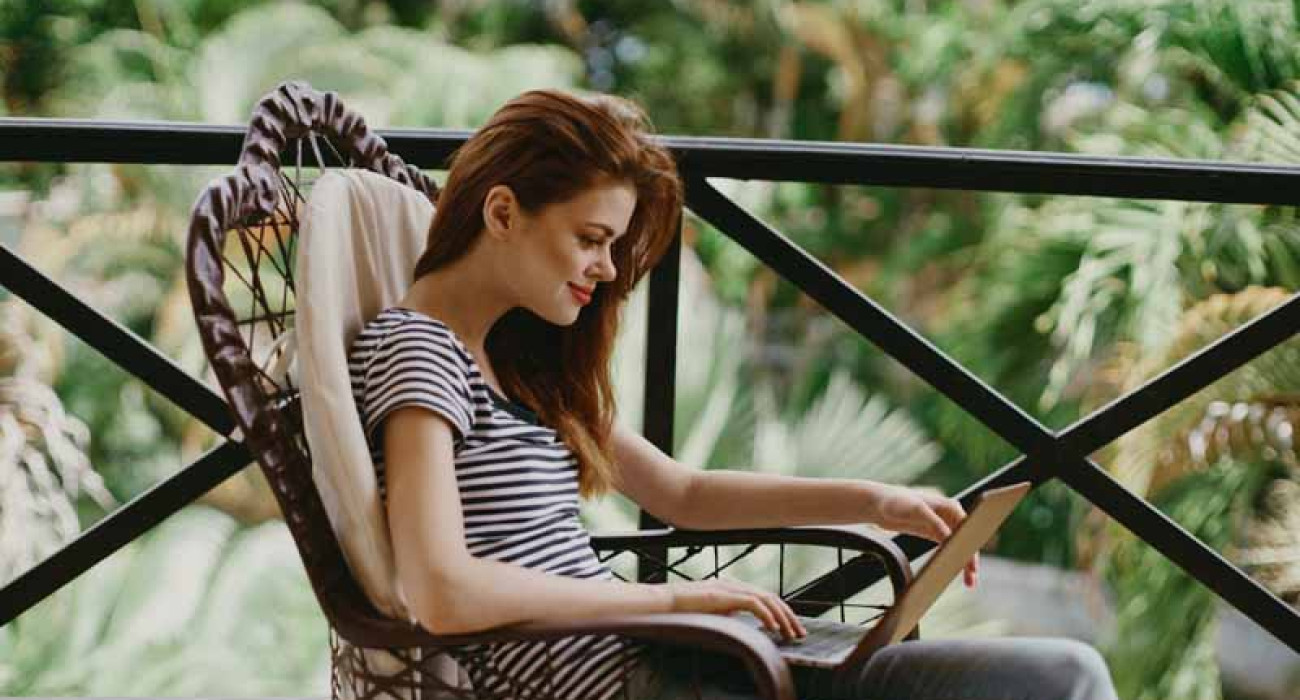 woman on the balcony with a laptop in her hands and nature in the background freelancer