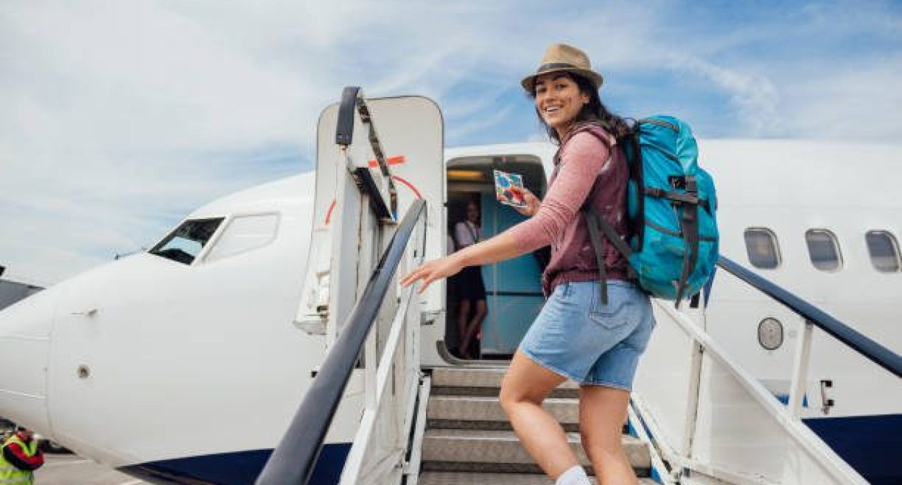 A young woman walking up steps while getting ready to board a plane at the airport in Toulouse, France. She is walking while looking back at the camera and smiling.