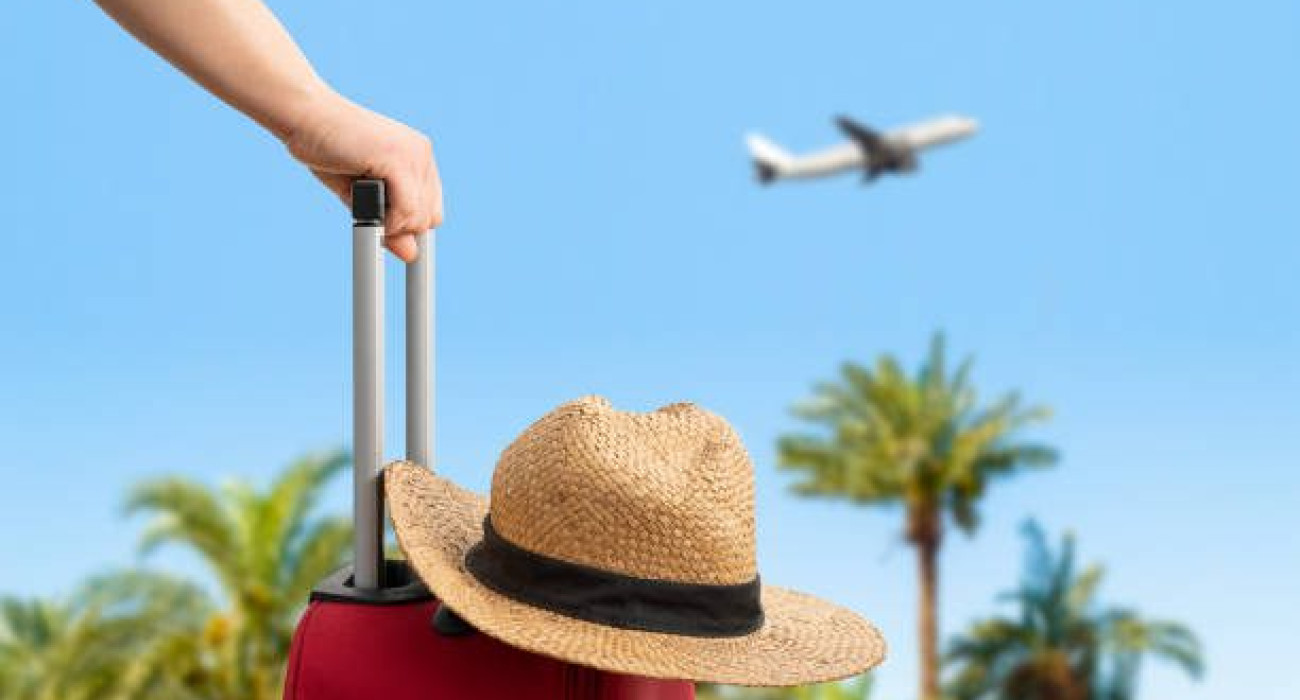 Woman with red suitcase standing on passengers ladder of airplane opposite sea with palm trees. Tourism concept