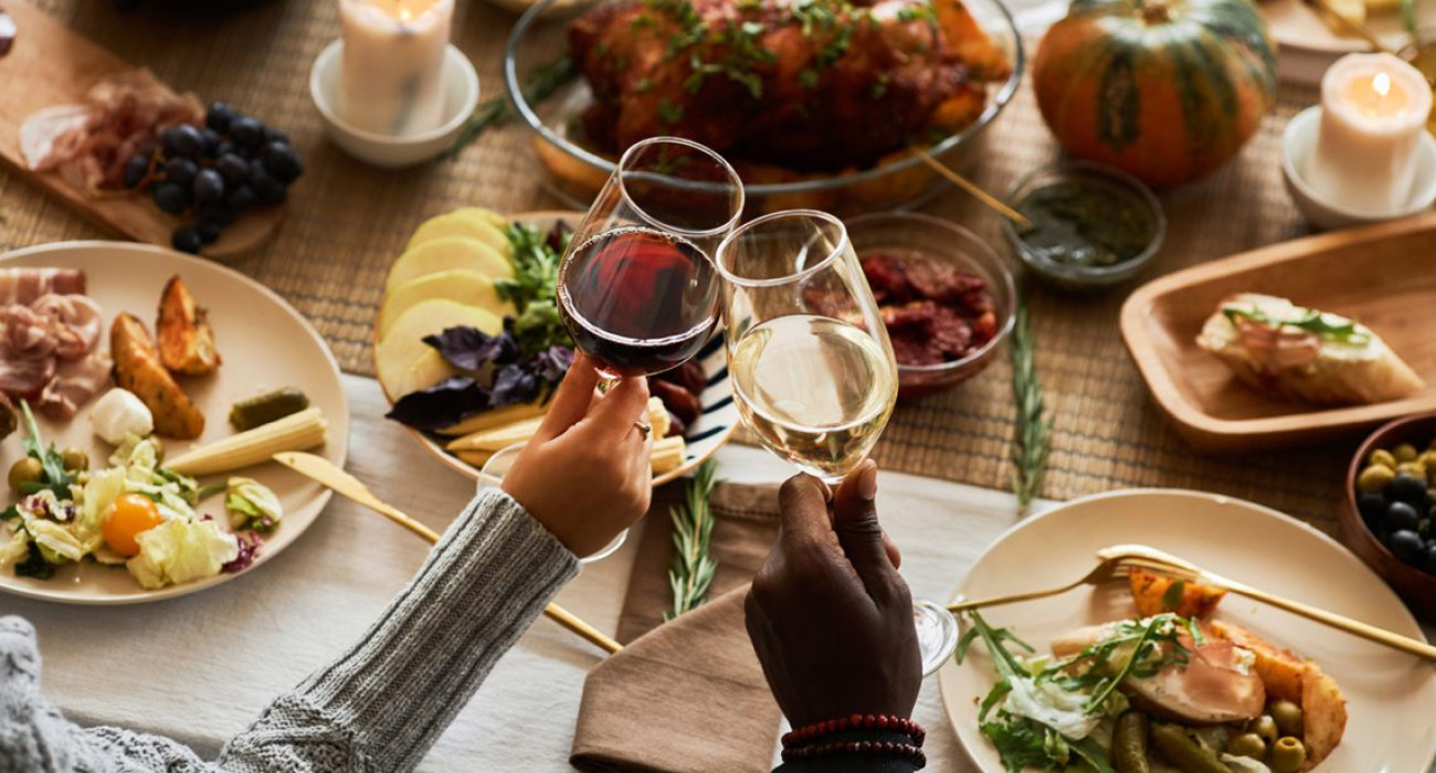 Close up of two people toasting with wine glasses at festive dinner table celebrating Thanksgiving with friends and family, copy space